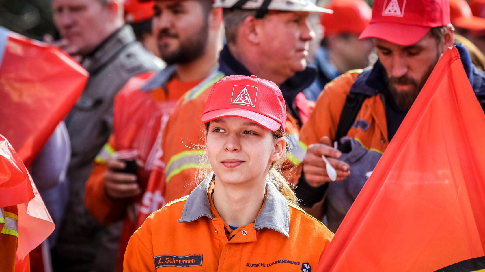 Eine junge Frau mit IG Metall-Kappe, einer Fahne und Arbeitskleidung auf einer Demo.