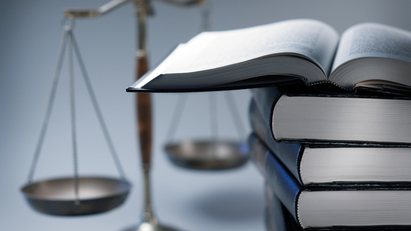 Ein Stapel voller Rechtsbücher mit Gesetzestexten liegt neben einer Richterwaage