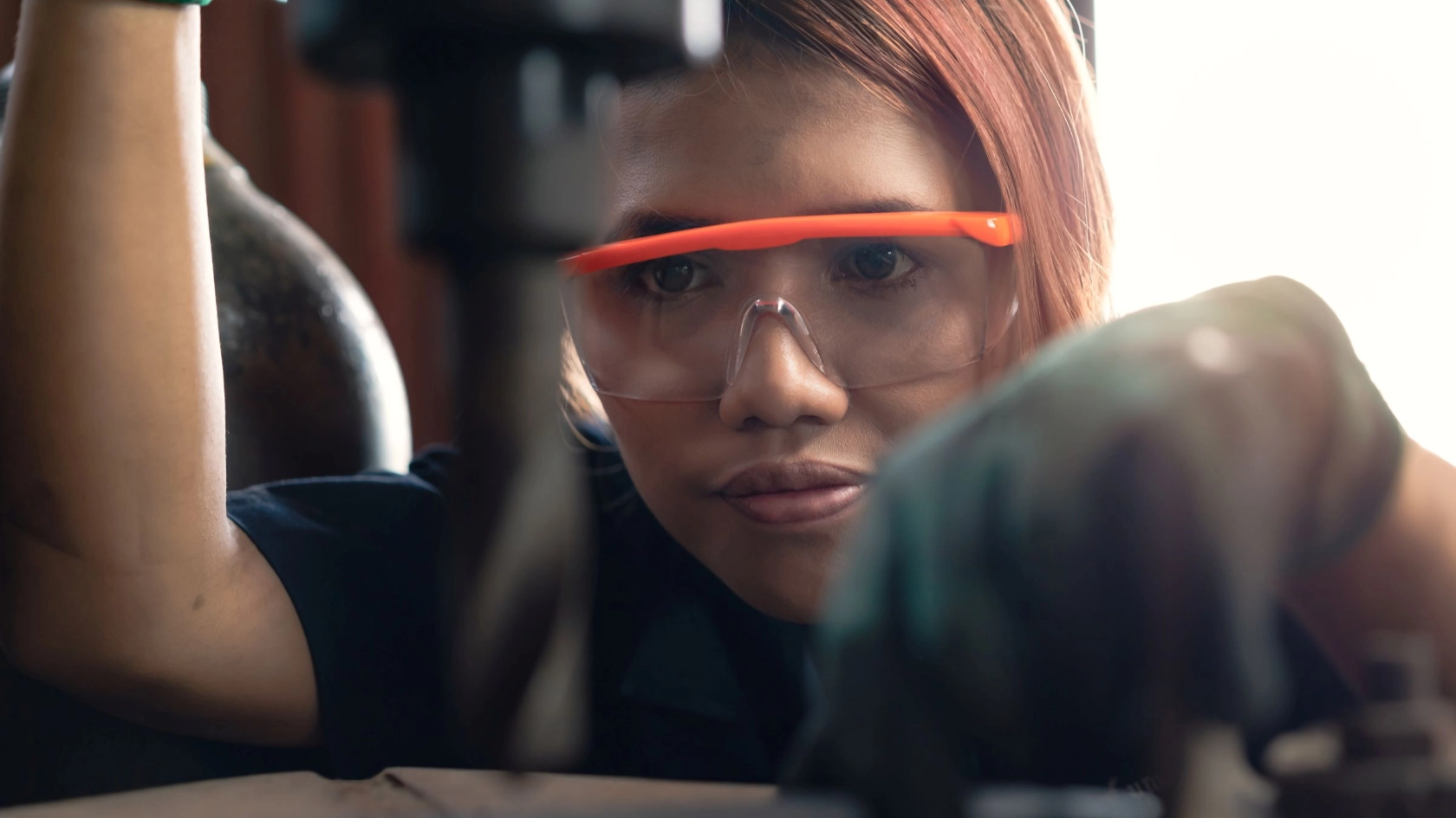 junge Frau arbeitet in einer Werkstatt mit Schutzbrille