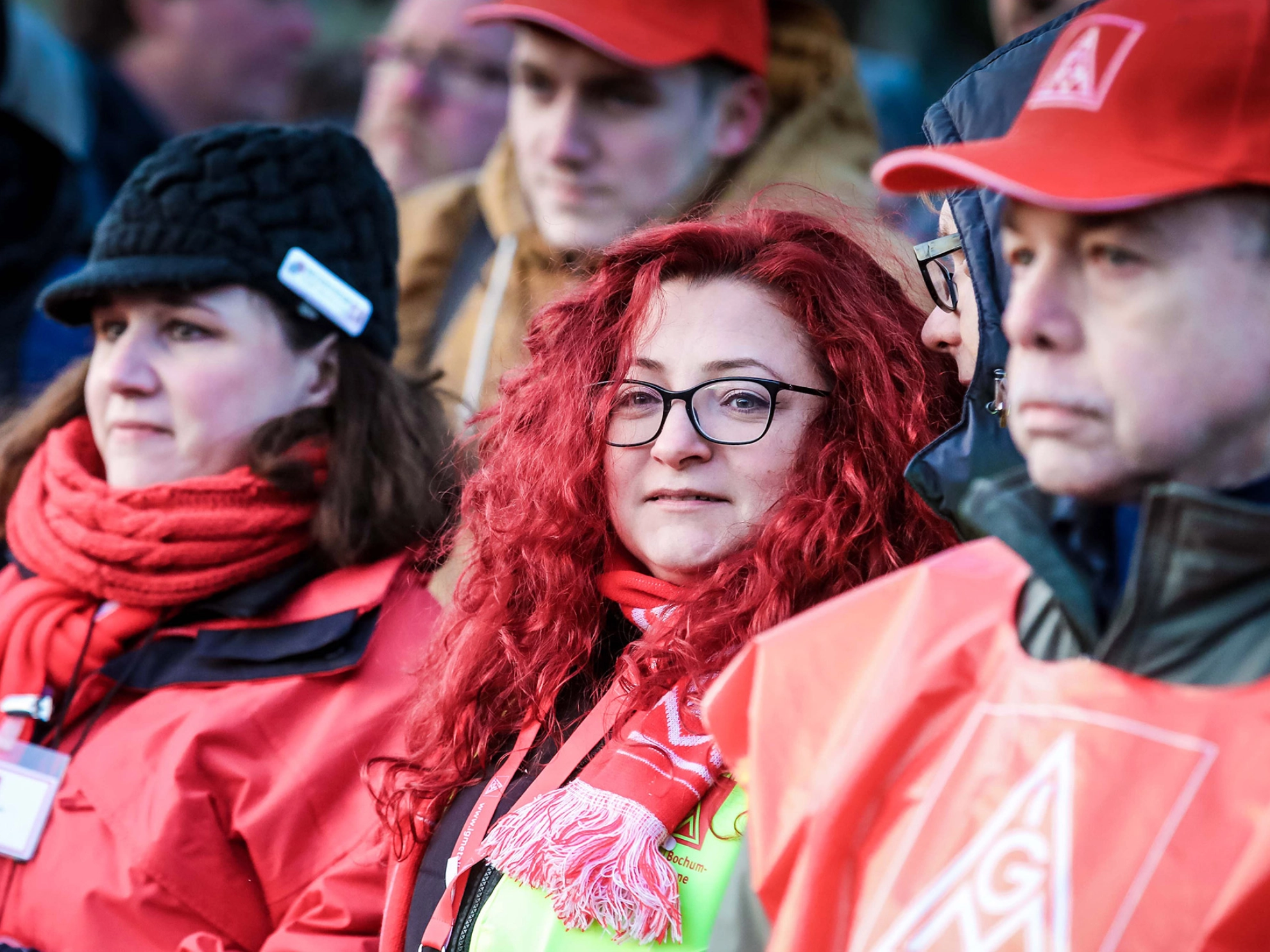 Eine Frau mit roten Locken, dunkler Brille und IG Metall-Schal lächelt in die Kamera.