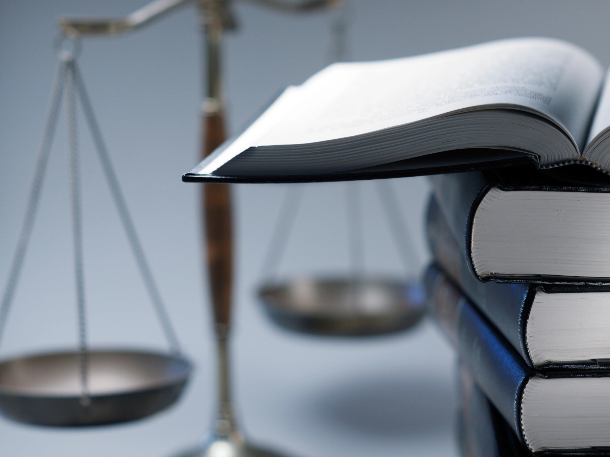 Ein Stapel voller Rechtsbücher mit Gesetzestexten liegt neben einer Richterwaage