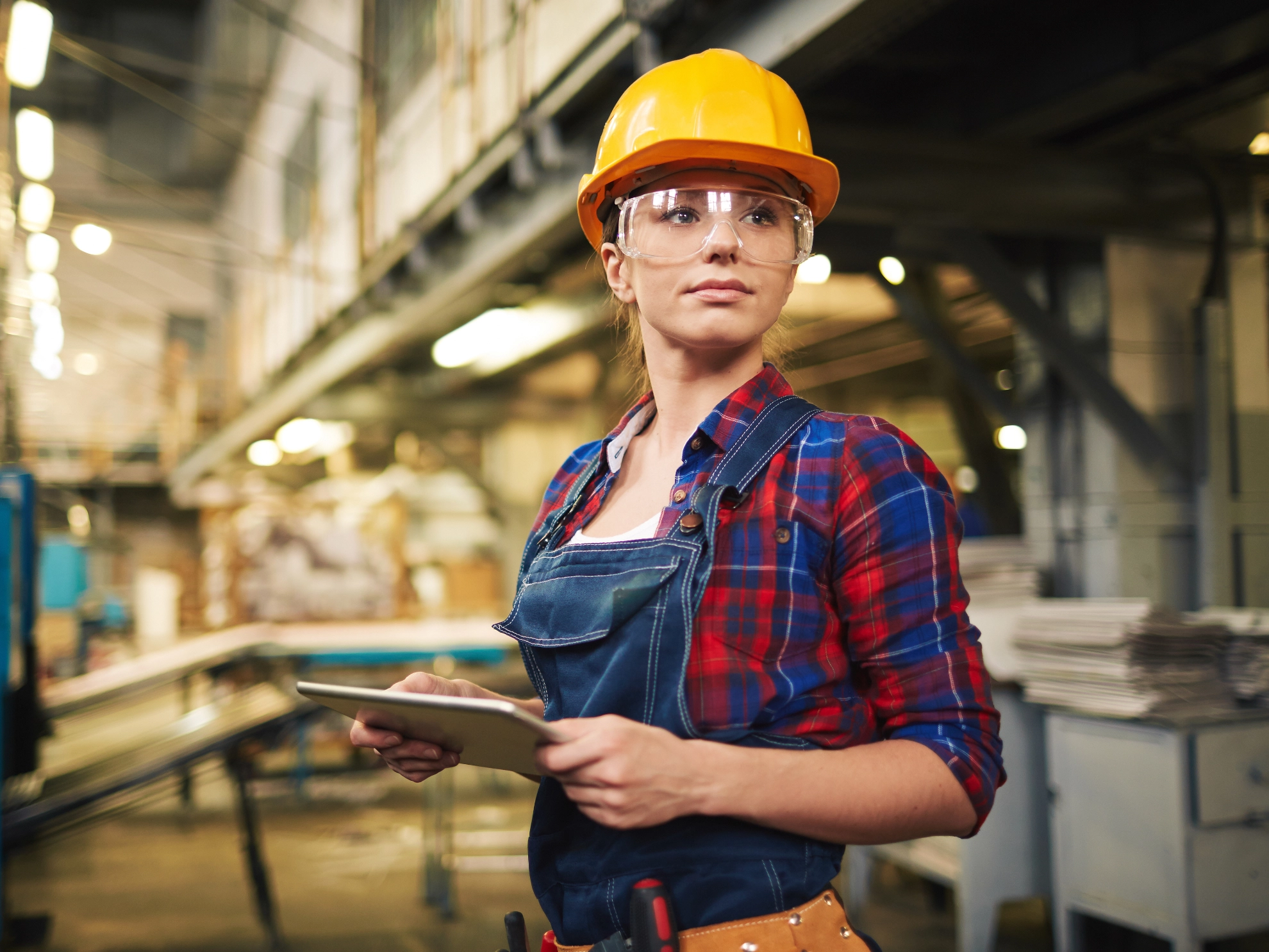 Eine junge Frau mit Schutzausrüstung und Tablet in einem Handwerksbetrieb.