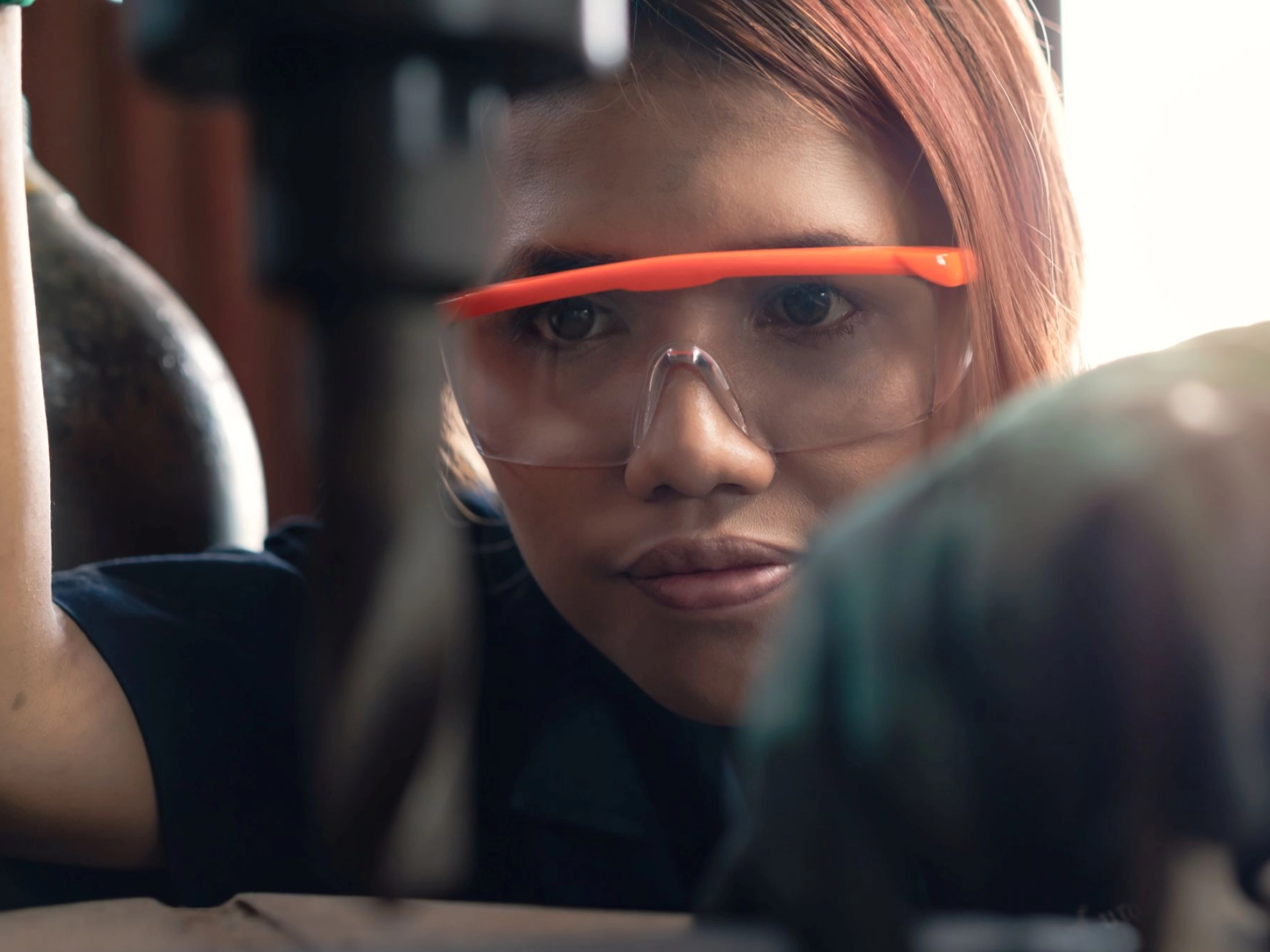 junge Frau arbeitet in einer Werkstatt mit Schutzbrille